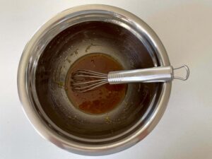 Brown sugar, olive oil, honey, vanilla extract, and salt in a stainless-steel mixing bowl with a whisk