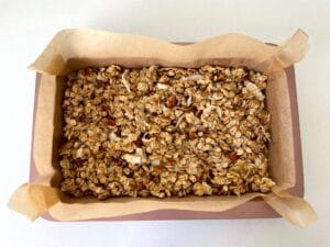 Granola mixture spread out in a rose gold slice tin ready to be baked