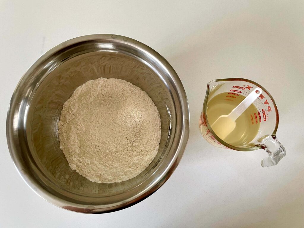 Ingredients including flour, salt, and yeast in a bowl and honey dissolved in water in a jug