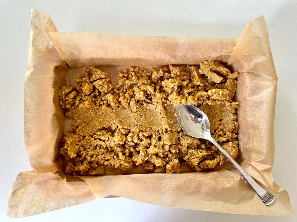 The biscuit base being pressed into the tin with a metal spoon