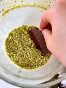 Chocolate pistachio Christmas tree cookie first dipped in chocolate and now being dipped in ground pistachios