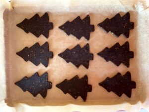 Chocolate pistachio shortbread dough that has been rolled out and cut into Christmas tree shapes