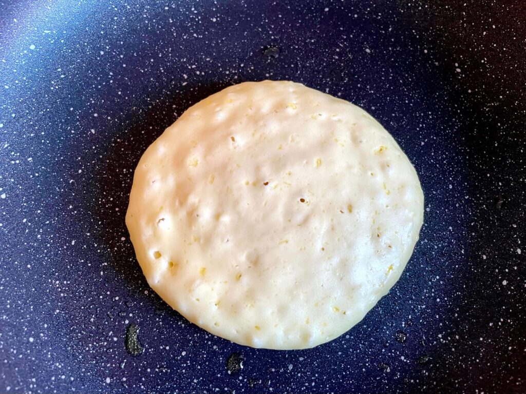 A pancake cooking in the frying pan with bubbles forming indicating that it's ready to flip
