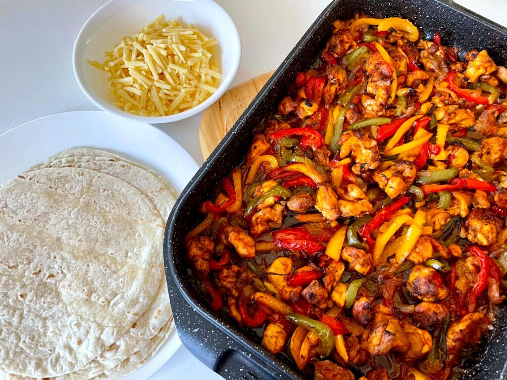 Sheet Pan Chicken Fajitas with a Plate of Tortillas and a Bowl of Shredded Cheese