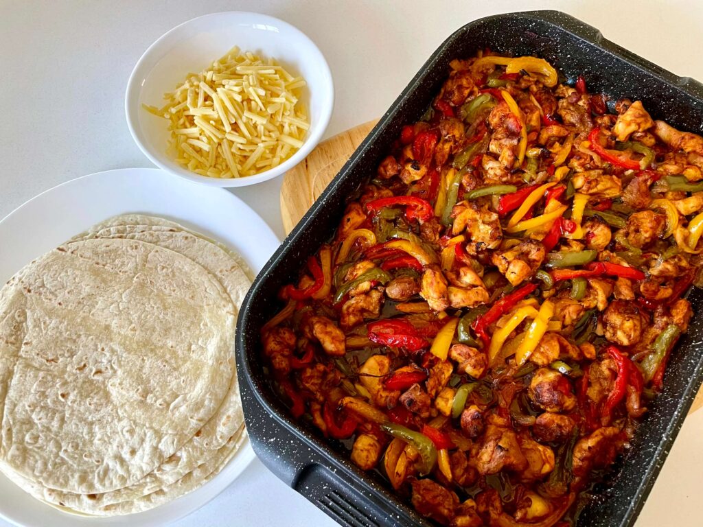 Sheet Pan Chicken Fajitas with a Plate of Tortillas and a Bowl of Shredded Cheese
